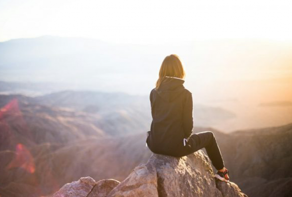 A girl setting on the top of a mountain 